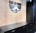 Logo kahvilan seinällä, puupaneeli tehosteseina ja logokyltti Cafe de Halle
